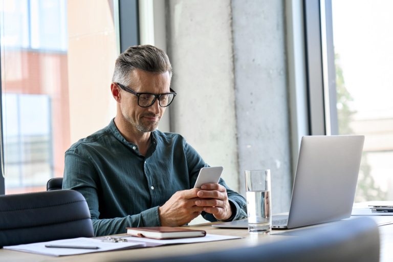 Smiling,Mature,Businessman,Holding,Smartphone,Sitting,In,Office