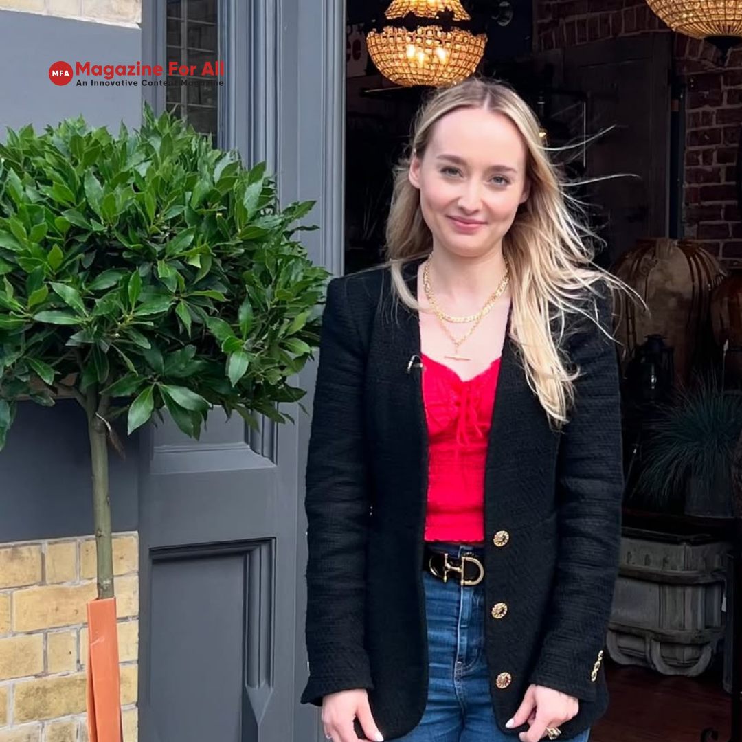 Hettie Jago dressed in jeans and a red top stands outside, looking confidently at the camera.