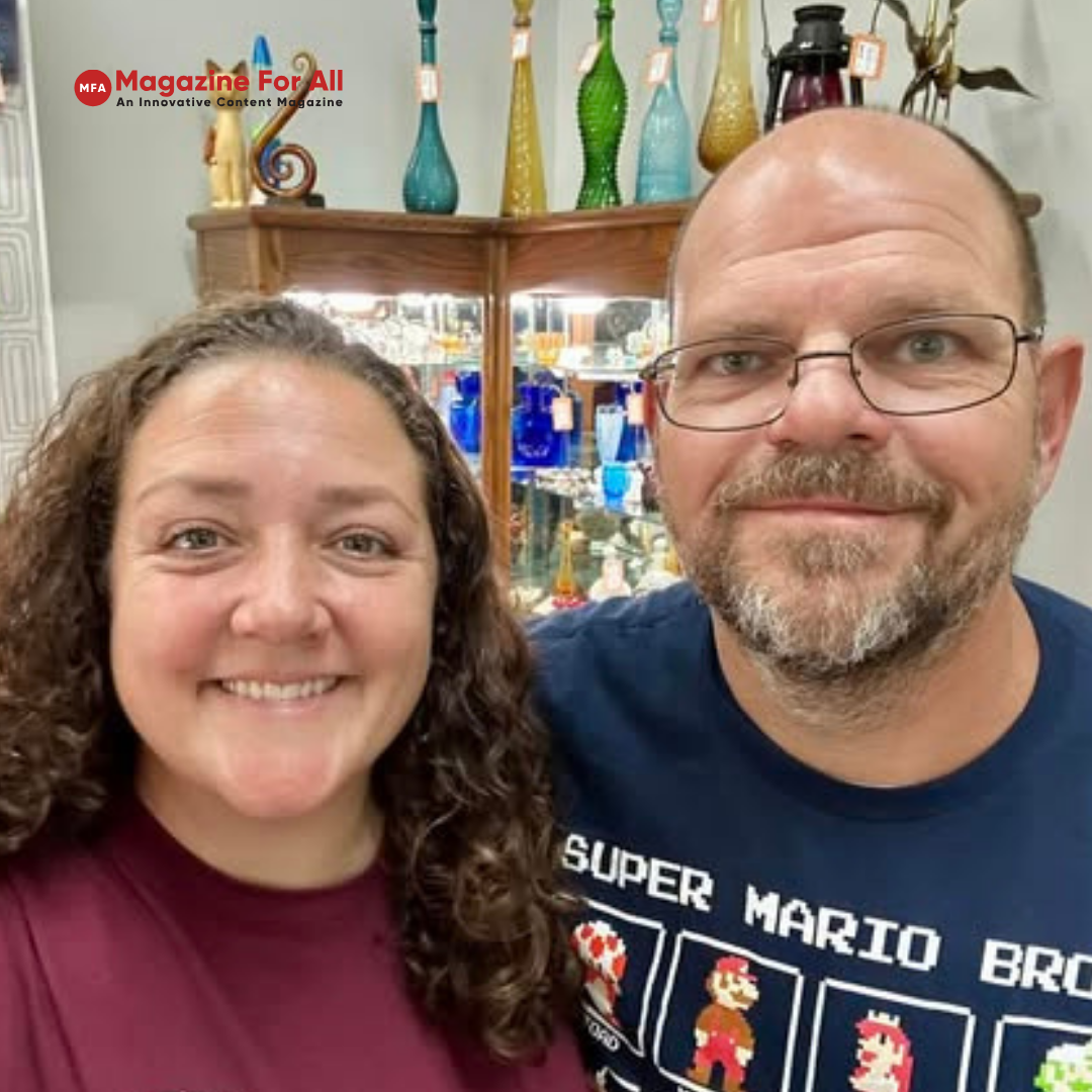 Jamie Veronica Murdock with Husband stand together in front of a shelf filled with various bottles.